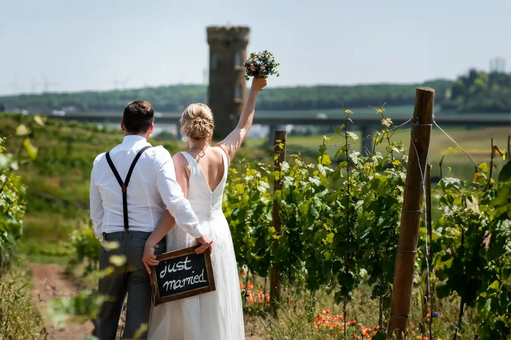 Brautpaar schaut in die Weinberge und halten ein Schild mit der Aufschrift just married.