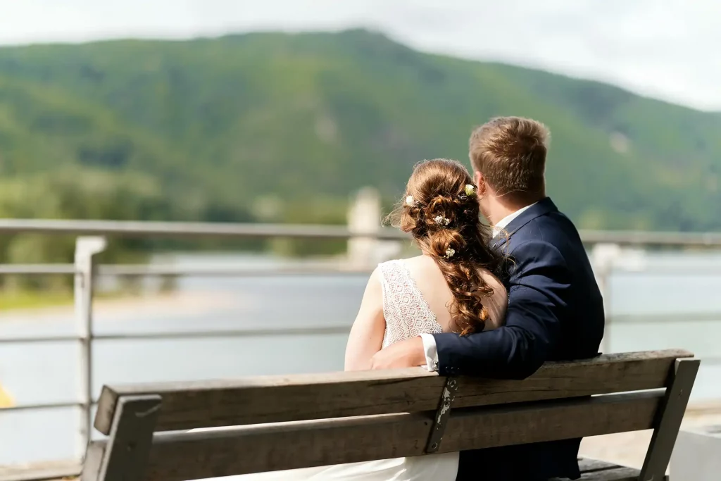 Brautpaar sitzt auf einer Parkbank und schaut aufs Rheinufer