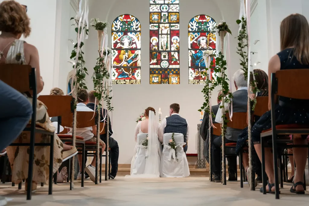 Brautpaar sitzt vor dem Altar mit der Hochzeitsgesellschaft
