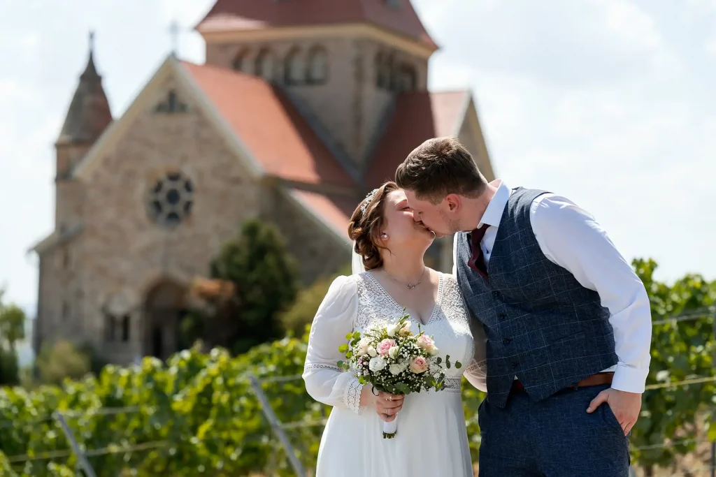 Brautpaar küsst sich vor der Kreuzkapelle Gau-Bickelheim