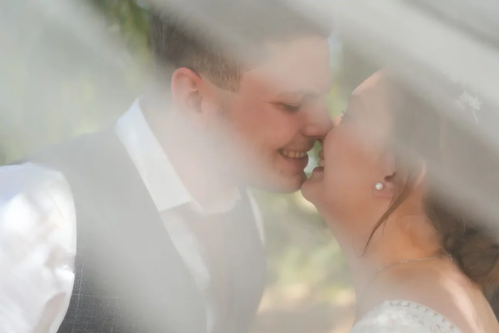Brautpaar küsst sich unter dem Schleider des Hochzeitskleids